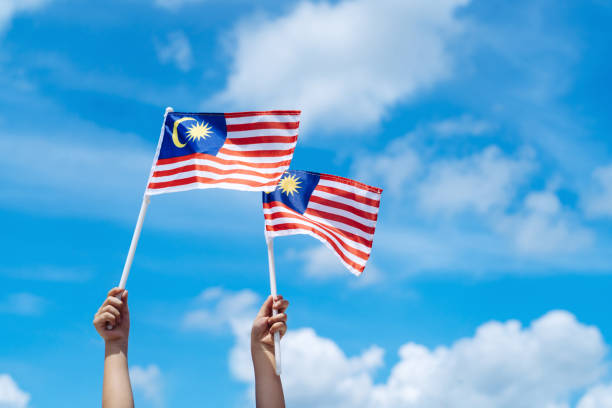 hand-happily-waving-malaysia-flag-against-blue-sky