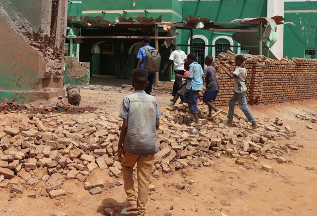 Children walk next to a collapsed mosque wall following a drone strike, at Khartoum North, in Bahri city